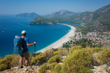 Fototapeta na wymiar Hiking on Lycian way trail. Man with backpack enjoy view of Oludeniz beach and Blue Lagoon from Lycian Way trail, Mediterranean coast in Turkey