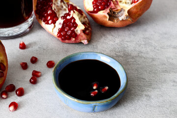 Pomegranate molasses in small bowl. Pomegranate sweet and sour syrup with pomegranate fruit and seeds on gray background.