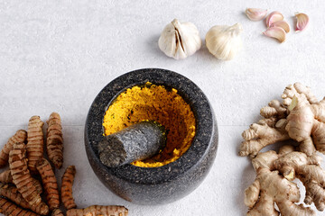 Pestle and mortar with garlic, ginger and turmeric paste with ingredients. Indian cuisine.