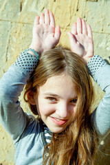 a teenage girl with long hair holds her hands above her head like bunny ears on a sunny day