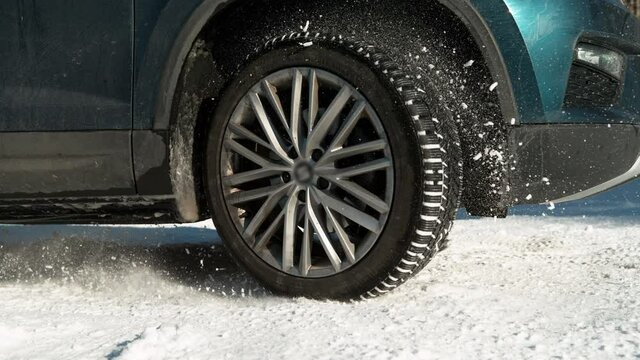 SLOW MOTION TIME WARP, CLOSE UP, LOW ANGLE DOF: Big blue SUV slips along the snowy road while trying to get traction. Vehicle's wheels are slipping and throwing up snow while driving along winter road