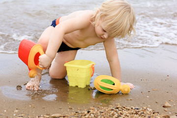 Little boy playing on the beach with plastic toys. Summertime, vacation, travel, childhood concept.