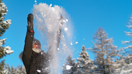 COPY SPACE, DOF: Smiling woman throws snow in air and outstretches her arms.