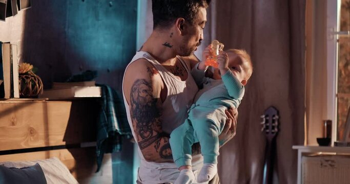 Tattooed dad puts the baby to sleep late at night, dad and son in the bedroom at night. 