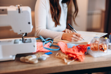 Young dressmaker woman is writing down ideas close-up. Creating online clothing design courses.