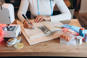Tailoring, sewing and clothing concept - close up of female fashion designer writing down ideas or...