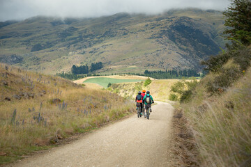 Obraz premium Three people cycling the Otago Central Rail Trail among mountain ranges between Waipiata and Middlemarch, South Island, New Zealand