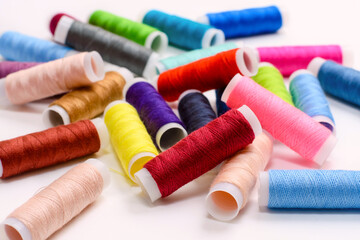 Many multi-colored spools of thread for sewing on a white background. The coils are scattered randomly. Selective focus in the foreground