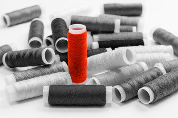 Lots of scattered black and white spools of thread and one red one. One spool of thread stands out...