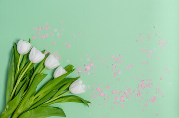 Bouquet of white tulips with colored confetti on a green background with copy space.