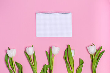 A bouquet of white tulips with a blank notebook for notes on a pink background