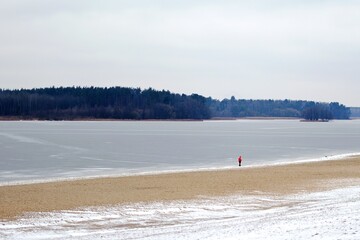 lonely person on deserted beach by frozen pond in winter