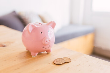 A pink piggy bank next to some gold coins on a modern wooden table in an office