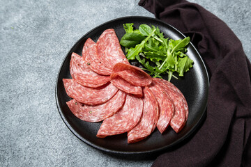 Salami with bread and arugula on a black plate.  top view. Ingredients for a salami sandwich. Elegant serving of snacks in the restaurant