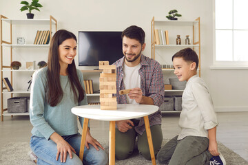 Happy young family with child enjoying free time on weekend and playing jenga board game at home....