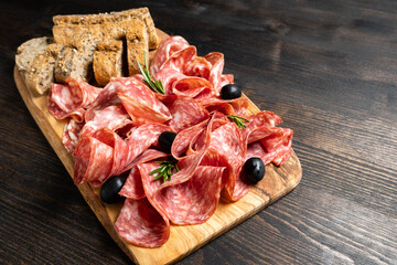 Sliced salumi salami on a wooden board with olives and multigrain baguette.  italian food, appetizer for aperitif or salami sandwich. Top view