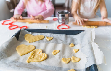 Little girls, sisters cooking homemade heart shaped cookies for valentine's day. Holiday for all lovers. Gift, surprize for mom. Red molds, rolling pin, flour, dough.Handmade family, bakery with kids