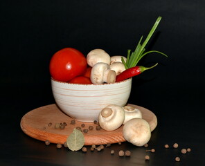 Fototapeta na wymiar red tomatoes, mushrooms, garlic, red hot pepper in a plate, allspice on round wooden board on a dark background. Space for text