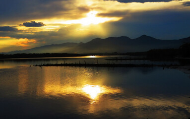 Obraz premium Orange sunset with rays over the mountains and reflections in the lake
