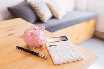 A pink piggy bank next to a white calculator and a black pen on a modern wooden table in an office