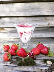 a glass bowl with  strawberries in cream on an old weathered wooden bench with berries spread out on it against the background of a gray fence . food wallpaper