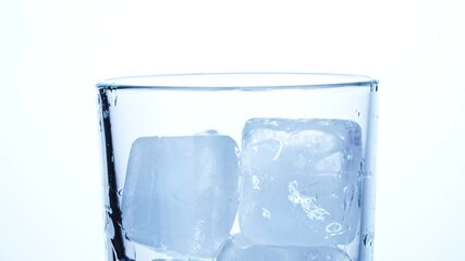 Close-up of ice cubes falling into an empty transparent glass on a white background. Slow motion. - Powered by Adobe