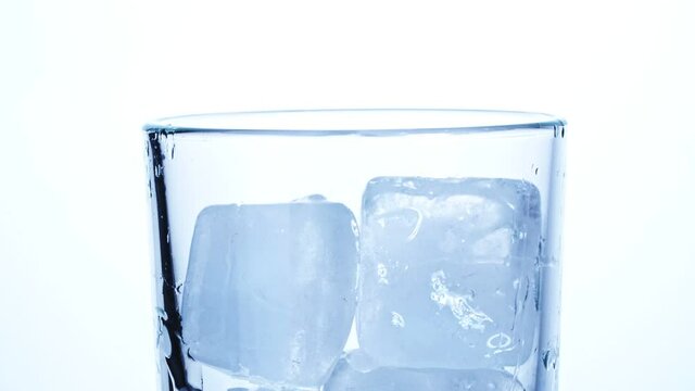 Close-up of ice cubes falling into an empty transparent glass on a white background. Slow motion.