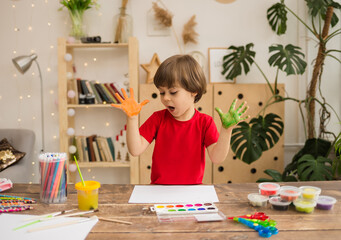 a little boy artist with painted palms sits at a table in the room