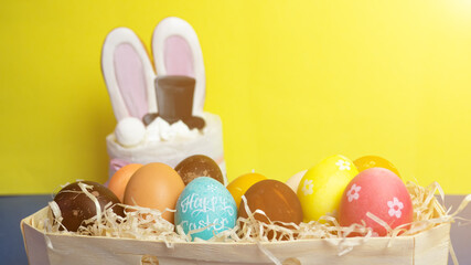 Easter cake decorated with bunny ears and black top hat, among colored Easter eggs in the hay