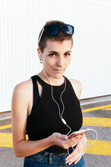 woman with short hair and piercings listening to music with headphones from her smartphone on the...