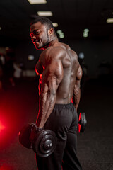 Fototapeta na wymiar View from the side on fit african american man with dumbbells doing workout at a gym. Sport, fitness, weightlifting, bodybuilding, training, athlete, workout exercises concept.