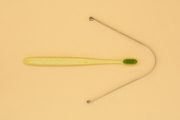 metal scraper or tongue cleaning brush and a toothbrush on beige background. Hygiene of the oral cavity