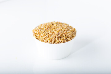 Uncooked bulgur wheat in white ceramic bowl isolated on white background.