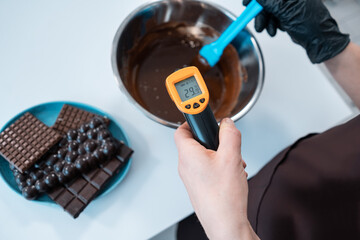 closeup of female measuring temperature of melted chocolate with pyrometer