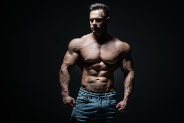 Fototapeta na wymiar young handsome sportsman bodybuilder posing in jeans on black background