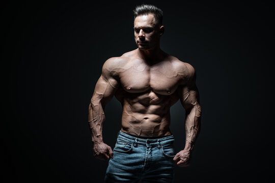 young handsome sportsman bodybuilder posing in jeans on black background