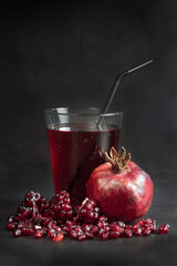 Natural pomegranate juice in a glass with ripe pomegranate fruit and juicy clusters of seeds on a black background.