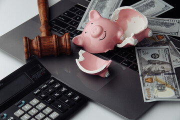 Broken pink piggy bank, cash and wooden gavel on laptop. Business and bankruptcy concept.