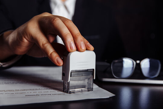 Person's hand stamping with approved stamp on document at desk. Business concept.
