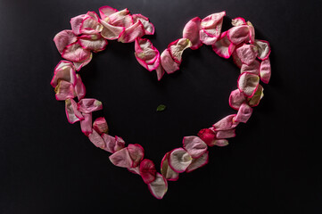 Red rose petals on a black background. Heart made of petals on a black background.