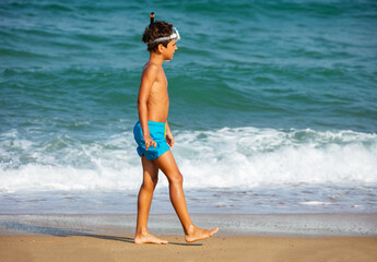 Portrait of a happy boy with scuba snorkeling mask walk in the sea waves