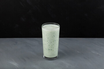 Fermented milk drink with herbs. Ayran or kefir with green basil and moringa leaves. Dark background, selective focus, copy space