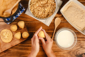 Hands of woman preparing brazilian croquette (coxinha de frango) on a wooden kitchen table