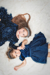 two cute baby girls sisters with blue eyes lie on their backs in blue dresses on faux fur