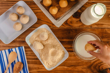 Hands of woman dipping brazilian croquette in milk (coxinha de frango) on a wooden kitchen table - Top view