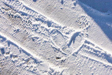 Couple's footprints in heart shape marked on white soft snow covering the road surface with natural sunlight. Abstract symbol and romantic message of love for winter season outdoor on Valentine's day.