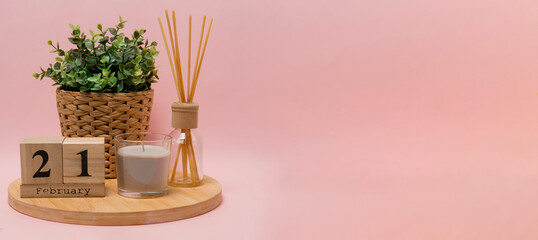 calendar. 21 february composition from a wooden calendar, a flower in a wicker pot, a gray candle in a glass candlestick and an aroma diffuser on a light pink background banner business