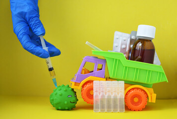 A woman wearing medical gloves gives an injection of the covid 19 coronavirus vaccine to a toy. Toys and a syringe on a yellow background. The medical concept of combating the covid-19 pandemic.