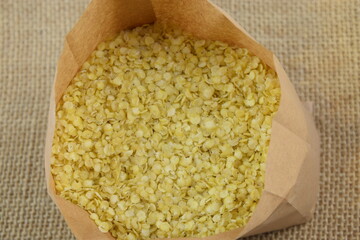 Millet flakes in paper bag closeup, gluten free healthy grains, on jute fabric background