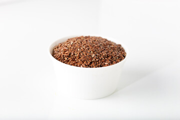 Flax seeds in white bowl on white background.
